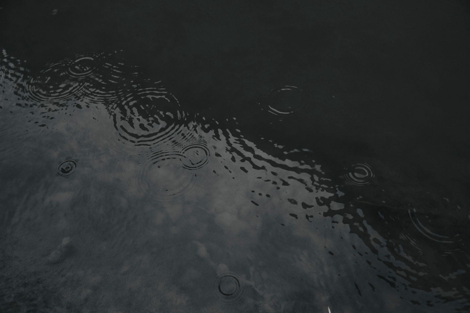 Raindrops forming concentric rings on the surface of dark, still water